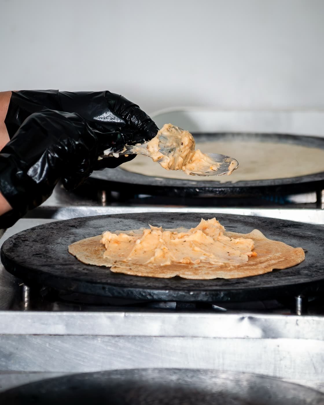 Recheio cremoso sendo espalhado sobre o crepe na chapa